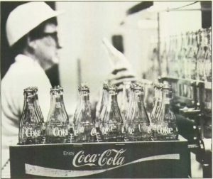 empty glass bottles in a coca cola container with a woman working in the background